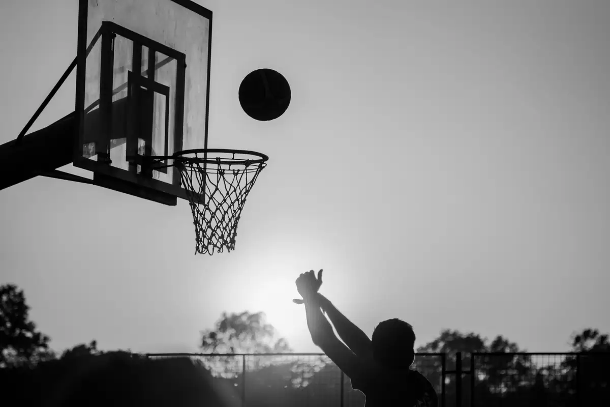 Un aro de básquet a contraluz al atardecer, con una pelota en el aire