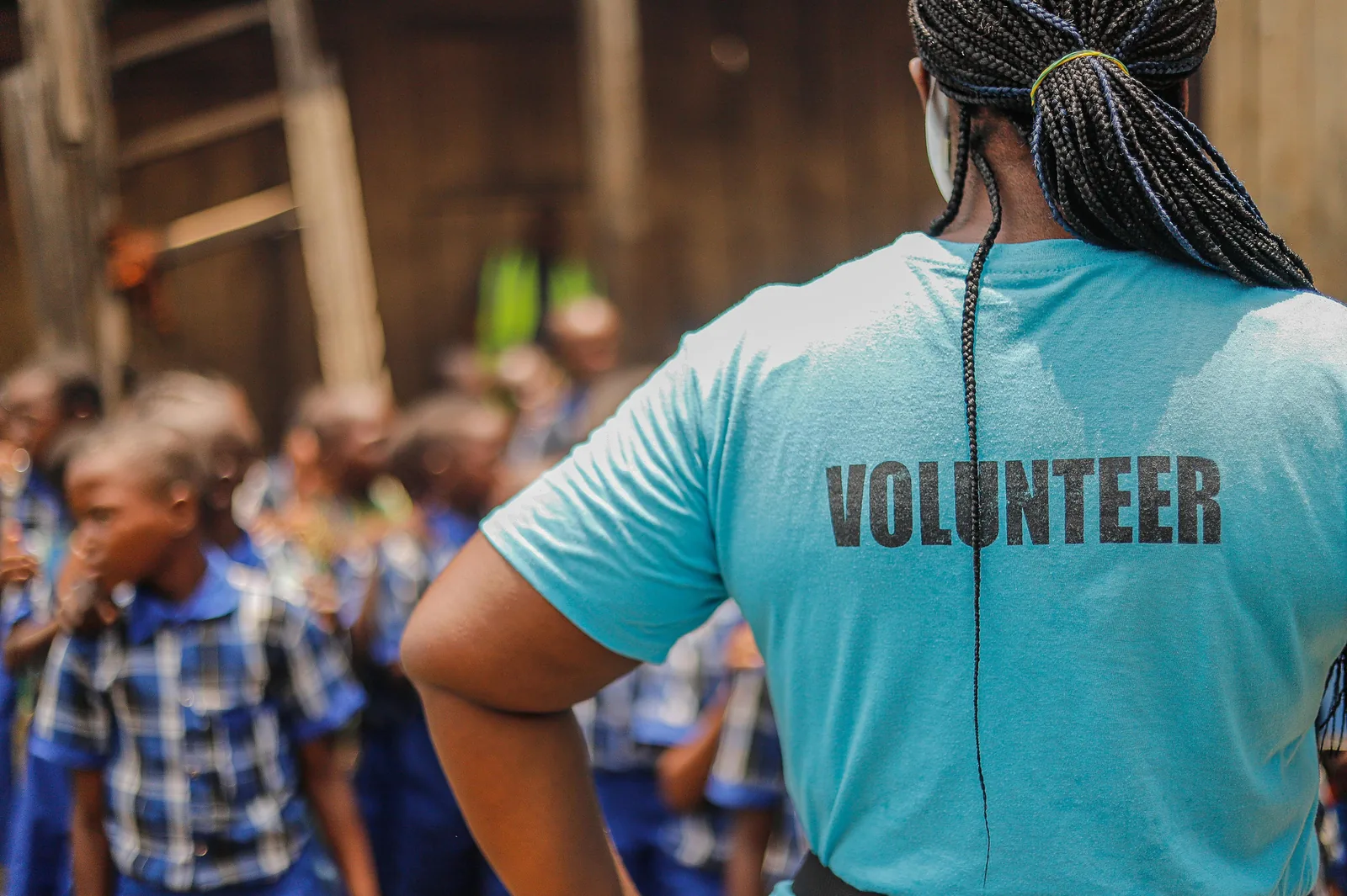Una voluntaria de espaldas, con la palabra VOLUNTEER en la remera, frente a un grupo de chicos